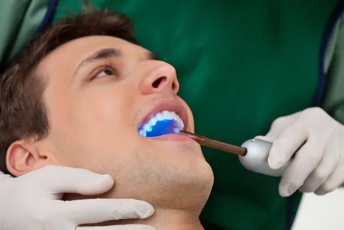 A dentist using a blue curing light inside a patient's mouth.