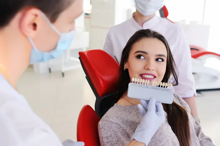 A dentist holds a tooth shade guide up to a smiling patient's teeth.