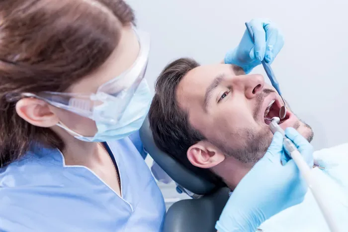 A dentist using dental instruments to examine the teeth of a patient in an exam chair.