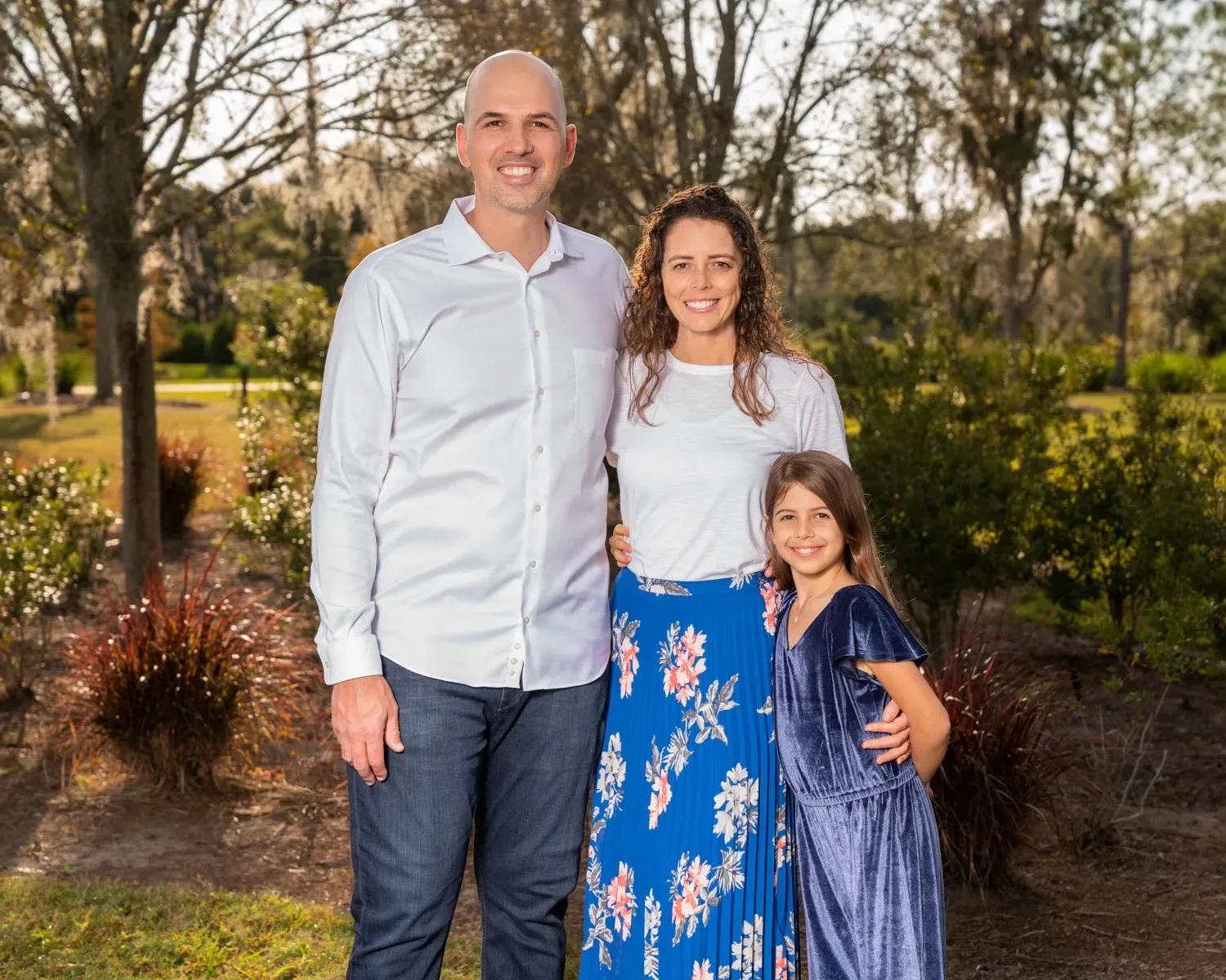 Two adults and a child smiling together outdoors in a park.